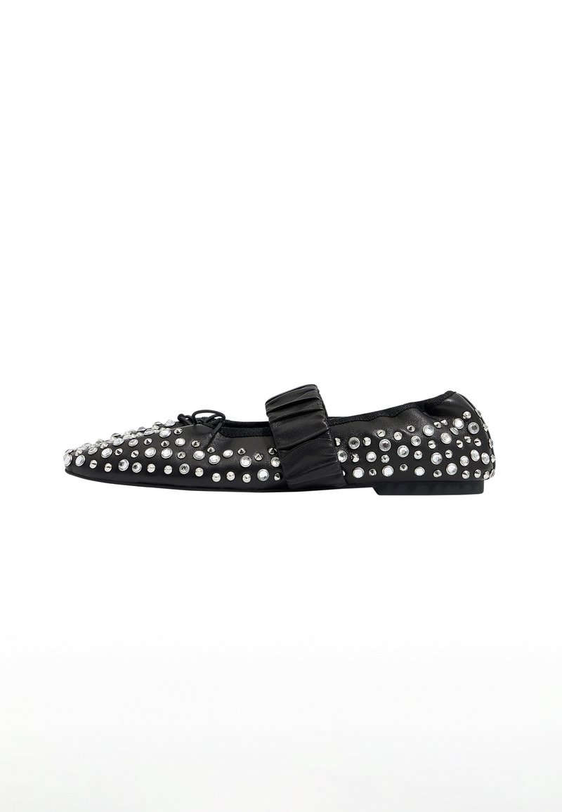 Zapato plano negro con punta afilada, adornado con tachuelas plateadas, presentando una correa de moño de satén en la parte superior. Textura suave y perfil bajo.