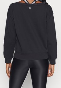 Sweat-shirt noir à coupe ample, col rond et poignets côtelés. Présente un logo dans le dos et est associé à des leggings noirs brillants.