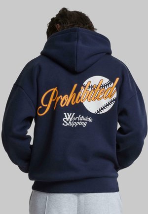 Mørkeblå hettegenser, myk stoff, med grafikk som sier "Forbudt" og "Verdensomspennende Frakt" med baseballdesign på baksiden. Tung kvalitet.