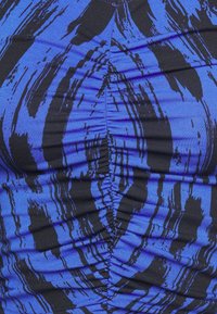 Pohled zblízka na modrou látku s černými abstraktními pruhy a centrálním řaseným švem, který vytváří zřasenou strukturu.