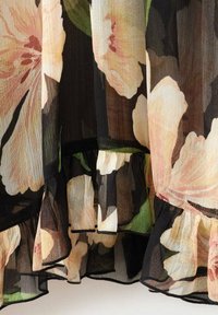 Tessuto di chiffon floreale con sfondo nero, caratterizzato da grandi fiori rosa e crema, orlo arruffato e bordo nero a contrasto.