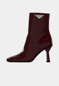 Bottine en cuir verni bourgogne avec un bout pointu, une silhouette élégante et un talon bloc unique avec un accent métallique triangulaire.