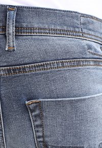 Jeans de mezclilla azul desgastados con costuras visibles, que incluyen un bolsillo trasero y pasadores para cinturón, con una textura suave y un diseño ajustado.