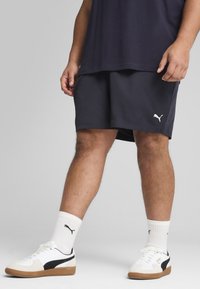 Sportovní outfit Puma s tmavě šedými šortkami a bílými teniskami s černými akcenty. Bavlněný materiál; zahrnuje logo Puma na šortkách a ponožkách.