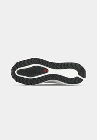 Semelle de chaussure de sport avec un motif de semelle en caoutchouc noir, mettant en vedette des accents blancs et un détail rouge près du talon. Surface texturée pour une meilleure adhérence.