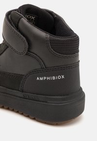 Černé kotníkové boty s texturovaným syntetickým svrškem, suchým zipem a gumovou podrážkou. Logo "Amphibiox" viditelné na patě.