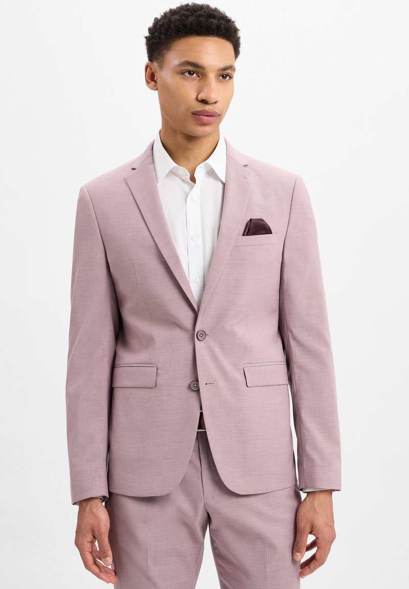 Lichtroze colbert met een getailleerde pasvorm, twee knopen, notch revers en een borstzak met een donkerpaars pochet. Witte dress shirt eronder.