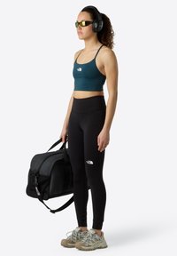 Vêtements de sport comprenant un soutien-gorge de sport teal et un legging noir taille haute. Les accessoires incluent des écouteurs noirs et un sac de sport noir.