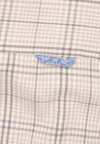 Geruite stof in beige en grijs met een gestructureerde afwerking. Heeft een blauwe accent met een geometrisch patroon en rafelige randdetails.