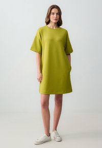 Abito verde a maniche corte realizzato in tessuto jersey, con una vestibilità comoda, scollatura rotonda e tasche laterali. Abbinato a sneakers bianche.