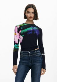 Ilgų rankovių marškiniai mėlynos spalvos audinyje su ryškiu gėlių raštu rožinės, žalios ir violetinės spalvų. Dėvimi su aukštu juosmeniu mėlynomis džinsinėmis kelnėmis su subtiliais akcentais.