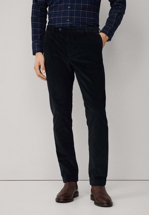 Donkerblauwe corduroybroek met een slim fit, voorzien van zijzakken en een knoopsluiting, gecombineerd met bruine leren enkellaarsjes.