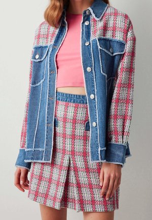 Femme portant un crop top rose, une jupe à carreaux et une veste à carreaux assortie avec des panneaux en denim et des boutons argentés.