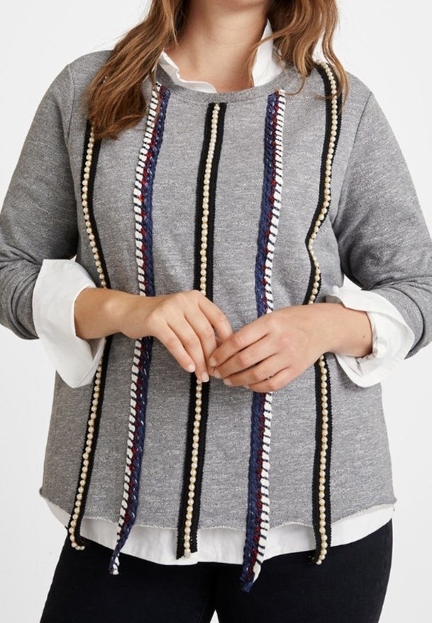 Grauer Pullover mit vertikalen Verzierungen in Schwarz, Marineblau und Creme, mit Rundhalsausschnitt und langen Ärmeln über einem weißen Hemd.