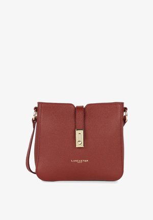 Sac bandoulière en cuir rouge avec une forme structurée, une fermeture à bascule dorée et une bandoulière amovible. Présente un logo de marque en relief sur le devant.