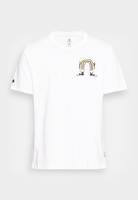 Camiseta blanca de algodón con cuello redondo. Presenta un gráfico impreso de un arcoíris sobre el texto "FAMILIA" y "UNIDAD" con dos zapatos de dibujos animados en la parte inferior.