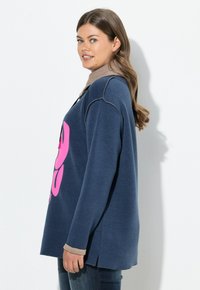 Nadmiernie duża granatowa bluza z dużym różowym nadrukiem. Posiada okrągły dekolt, boczne rozcięcia oraz kontrastowe beżowe wykończenie mankietów.