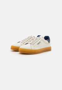 Hvite lær sneakers med teksturert overflate, blå detaljer på hælen og chunky oransje gummisåle. Har klassisk snøring.