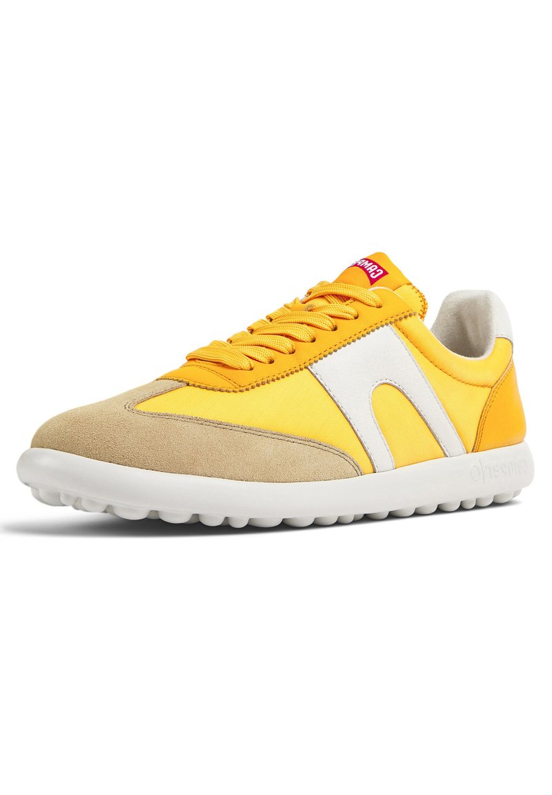 Zapatillas amarillas y beige con materiales de ante y nailon. Presentan un panel de acento blanco, cordones redondos y una suela de goma blanca texturizada.