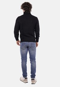 Maglione a collo alto navy a maglia con orlo a coste, abbinato a jeans blu chiaro e scarpe da ginnastica grigie, ripreso da dietro.