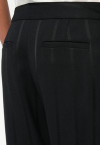 Melni piegriezti bikses ar teksturētu audumu un smalkiem svītrojumiem, taisna griezuma, divām aizmugurējām kabatām un gludu jostasvietu.