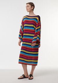 Multicolor gestreepte gebreide jurk met brede mouwen, een losse pasvorm en een lengte tot de knieën. De strepen zijn in rood, blauw, geel en paars.