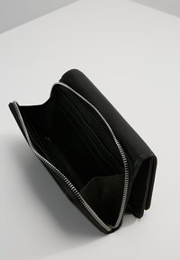 Czarny skórzany portfel z srebrnym zamkiem błyskawicznym, otwarty, ukazujący wiele przegródek na karty oraz przestronne wnętrze. Gładka tekstura, elegancki design.