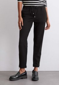 Zwarte joggingbroek met elastische tailleband en trekkoord, met ritsdetails bij de boorden en een gladde, gestructureerde stof.