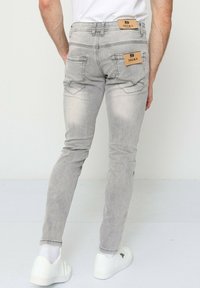 Jeans skinny gris avec une texture délavée, dotés de deux poches arrière et de deux étiquettes en cuir. Portés avec des baskets blanches et des chaussettes mi-mollet.