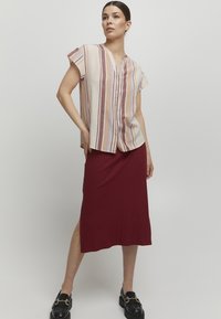 Chemise à manches courtes avec boutons et rayures verticales en beige et mauve, associée à une jupe midi bordeaux avec une fente sur le côté et une texture côtelée.