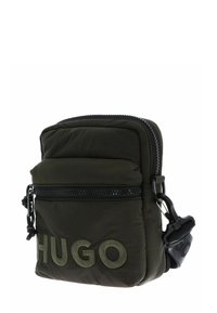 Piccola borsa a tracolla imbottita di colore verde scuro con tasca frontale con zip e "HUGO" ricamato sul davanti con filo verde dello stesso colore.
