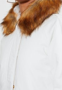 White jacket featuring a faux fur collar in shades of brown, with a smooth texture and button closure on the front.