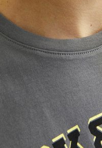 Grijze katoenen t-shirt met een ronde halslijn. Zwart en geel bedrukte tekst siert de voorkant, met zichtbare stiksels langs de kraag.