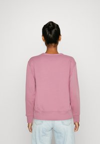 Sweat-shirt rose avec un col ras du cou et des poignets côtelés. Confectionné dans un tissu doux, il présente une coupe légèrement ample sans motifs visibles.
