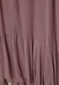 Tissu rose pâle et poussiéreux avec un design en couches ; présente un ourlet froncé et des coutures visibles pour texture et détail.