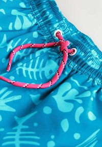 Pantaloncini da bagno turchesi con motivi a lisca di pesce e astratti, vita elastica e coulisse rosa infilata in un occhiello d'argento.