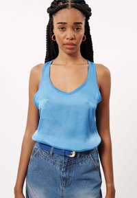 Lichtblauw mouwloos topje van een gladde stof, met een V-hals ontwerp. Gecombineerd met een denim rok en een blauwe riem.