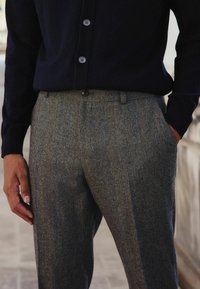 Gray herringbone trousers with a tailored fit and pockets, paired with a navy knit button-up shirt. Textured fabric, sleek design.