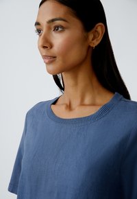 Blaues kurzärmliges Oberteil aus glattem Stoff, mit einem runden Ausschnitt und gerippten Abschlüssen, in lockerer Passform und mit subtiler Textur.