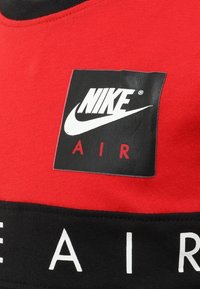 Nike Air logo patch in het wit en rood op een zwart en rood stoffen achtergrond, waarschijnlijk onderdeel van een sportkledingstuk.