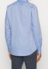 Světlomodrá košile s dlouhým rukávem vyrobená z hladké látky. Má límec, manžety na knoflíky a rovný lem. Bez viditelných vzorů nebo ozdob.