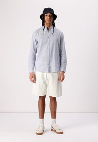 Stripet skjorte i blå og hvid, parret med hvide shorts. Sort bucket hat, hvide sokker og beige sneakers fuldender outfittet.