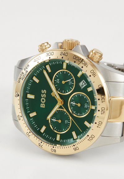 Montre en acier inoxydable doré et argenté avec un cadran vert, des accents dorés, trois sous-cadrans et un affichage de la date à 4 heures.