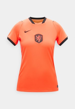 Jasnopomarańczowa sportowa koszulka z krótkim rękawem z czarną obwódką, czarnym herbem lwa na piersi i czarnym logo Nike po prawej stronie.