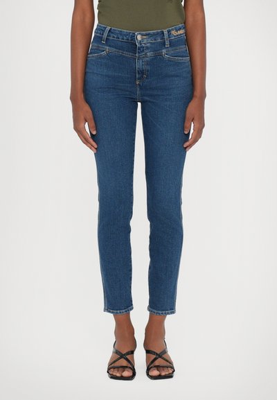 Høj talje mørkeblå jeans med slim fit, med forlommer og en subtil syning, parret med sorte stroppsandaler.