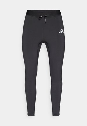 Schwarze, sportliche Leggings aus elastischem Stoff, mit einem Tunnelzugbund und einem weißen Logoakzent am linken Oberschenkel.