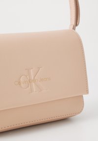 Torebka Calvin Klein Jeans w delikatnym różowym skórzanym wykończeniu, z wytłoczonym logo, gładką fakturą, minimalistycznym designem oraz subtelnym akcentem metalowym.