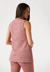 Ärmlös topp i en strukturerad rosa stickad tyg, med rundad halsringning och en avslappnad passform, ihop med matchande mönstrade bottnar.