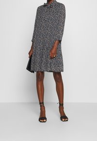 Black floral print dress with long sleeves and a collar. Lightweight fabric, flowing silhouette, paired with black strappy sandals and a clutch.
