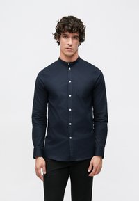 Μπλε ναυτικό πουκάμισο με κουμπιά, υψηλό γιακά, μακριά μανίκια και τσέπη στο στήθος· διαθέτει αντίθετα λευκά κουμπιά και λεία υφή υφάσματος.